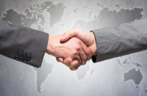 Two Men Shaking Hands in Front of Gray Global Map