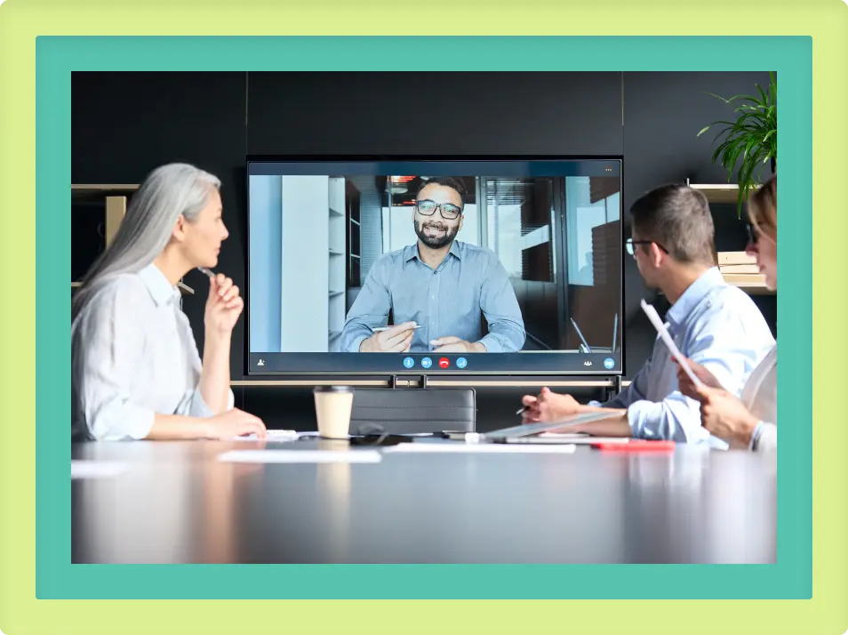 A group of people sitting at a table looking at a man on a television